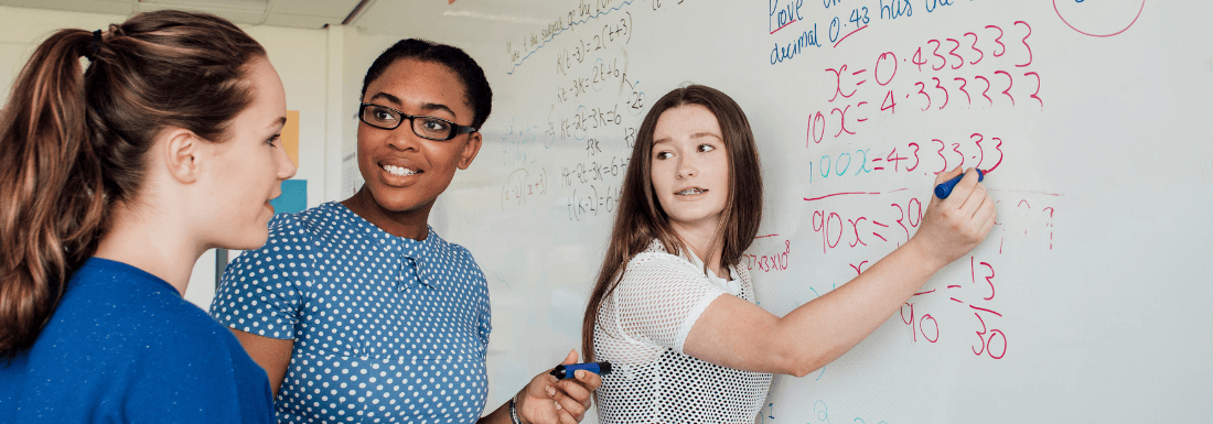 Two white female young adults and their black female teacher practicing math at a whiteboard