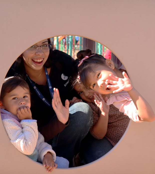 AmeriCorps member with three female preschoolers smiling and waving at the camera