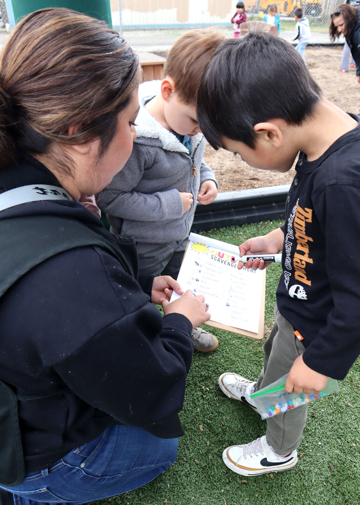 Teacher and Preschool Student outside looking down at a clipboard