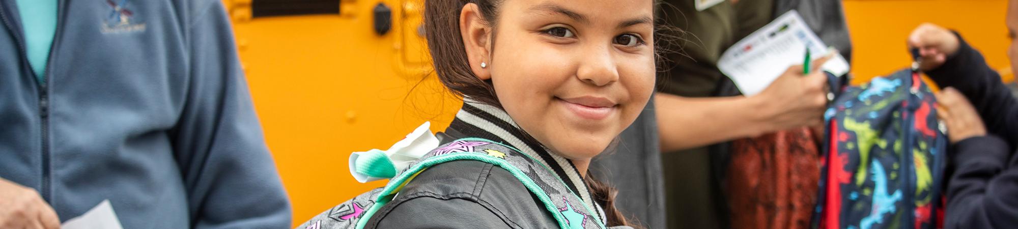 Girl with Backpack in front of school bus